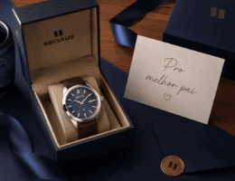 Caixa de presente Seculus aberta com relógio masculino em destaque e cartão escrito "Pro melhor pai", sobre fundo em tons de azul-marinho e madeira, em composição premium e afetuosa para o Dia dos Pais.