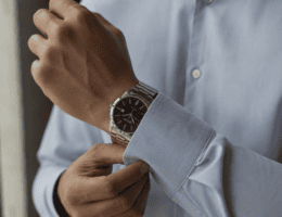 Homem ajustando o punho da camisa social enquanto usa um relógio Seculus em aço prata no pulso, com foco na proporção do relógio e iluminação natural lateral.