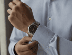 Homem ajustando o punho da camisa social enquanto usa um relógio Seculus em aço prata no pulso, com foco na proporção do relógio e iluminação natural lateral.