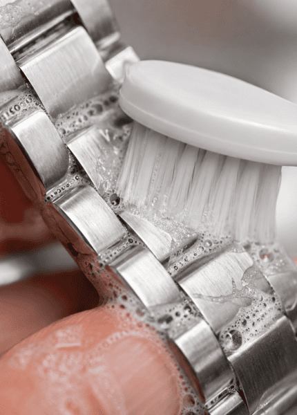 Escova de dentes extramacia limpando suavemente os elos de uma pulseira de aço com espuma de sabão.