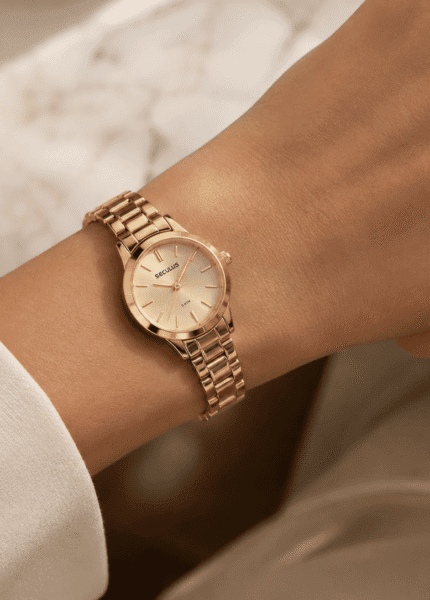 Pulso feminino usando relógio Seculus dourado de caixa pequena, combinado com anel solitário, em composição delicada e elegante.