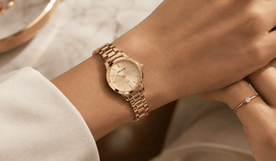 Pulso feminino usando relógio Seculus dourado de caixa pequena, combinado com anel solitário, em composição delicada e elegante.