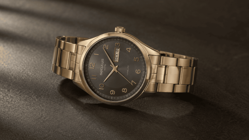 Relógio masculino Seculus analógico dourado com pulseira de elos em aço, mostrador cinza-chumbo com numeração completa e detalhes dourados, sobre superfície escura com luz natural lateral.