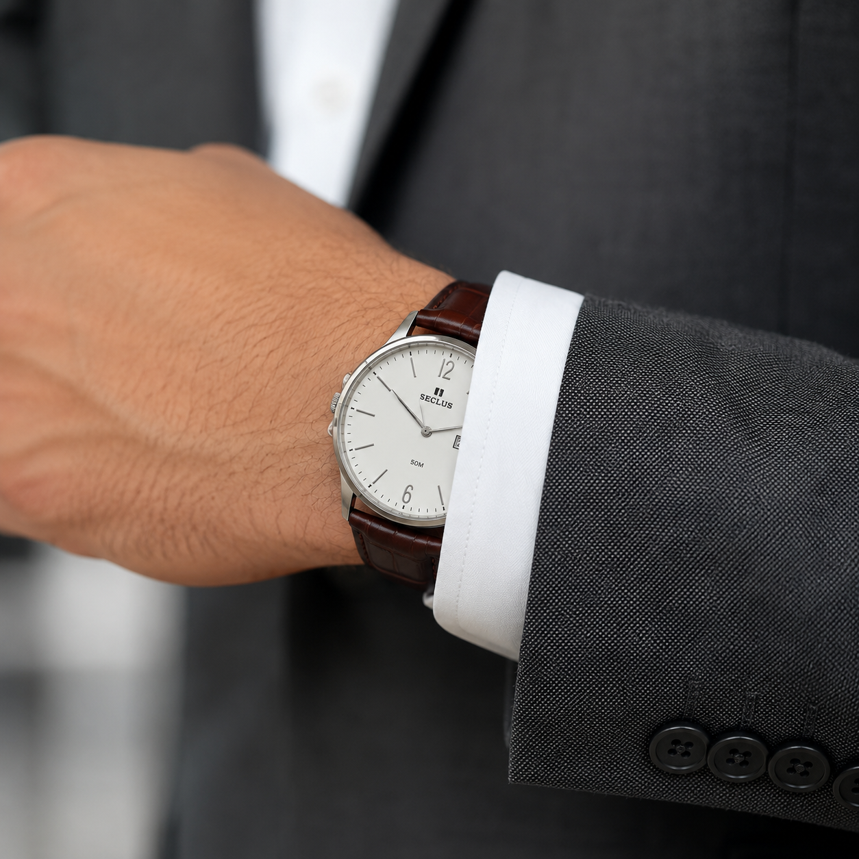 Close-up do pulso masculino com terno cinza e camisa branca, relógio Seculus de perfil slim deslizando discretamente sob o punho da manga, fundo desfocado