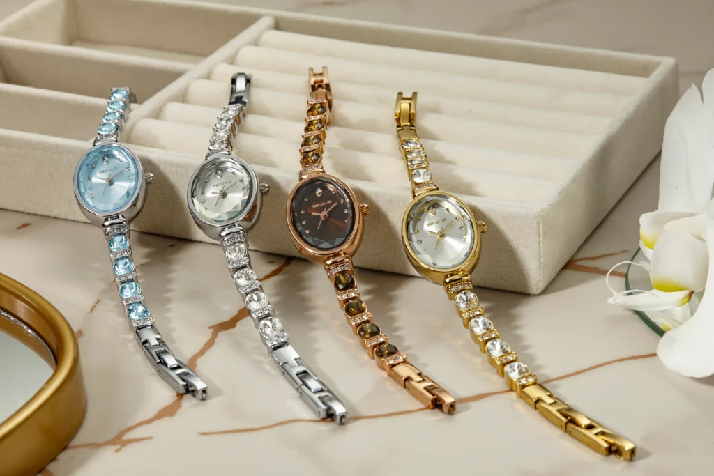 Disposição flat lay sobre superfície de mármore claro mostrando seis pulseiras de relógio lado a lado: couro marrom, couro preto, aço inoxidável, milanesa dourada, silicone preto e nylon NATO verde, com luz natural lateral