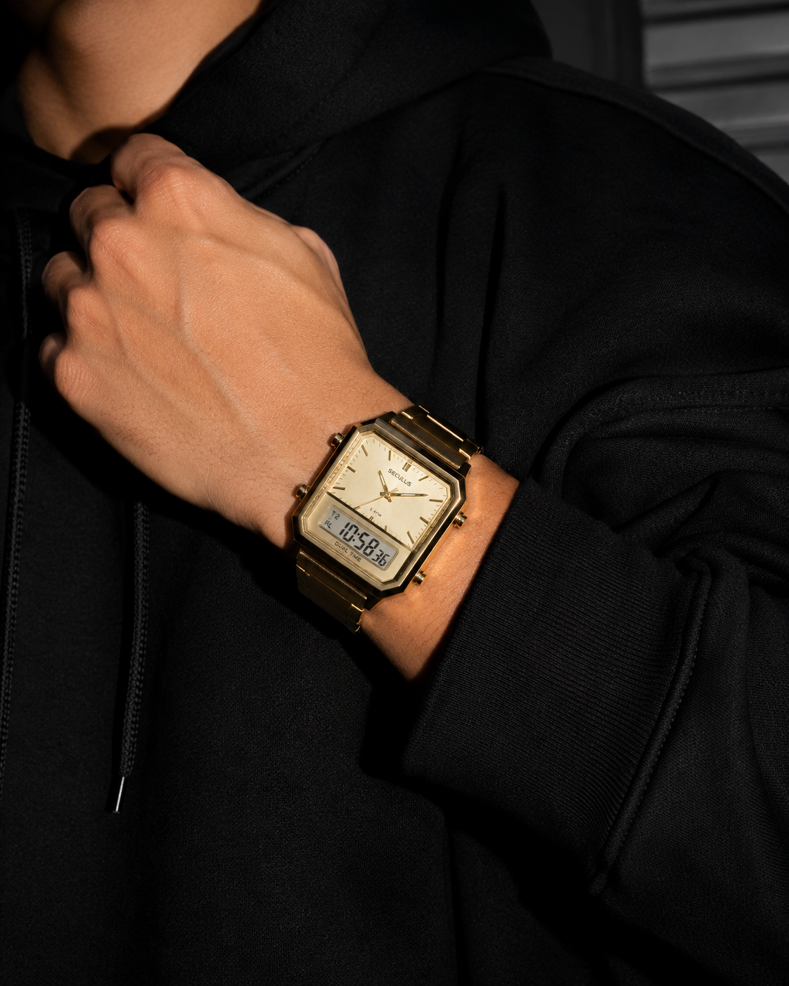 Homem usando relógio masculino Seculus Dual Time dourado no pulso sobre hoodie preto oversized, com iluminação de flash, alto contraste entre dourado e preto e foco no mostrador analógico e digital.