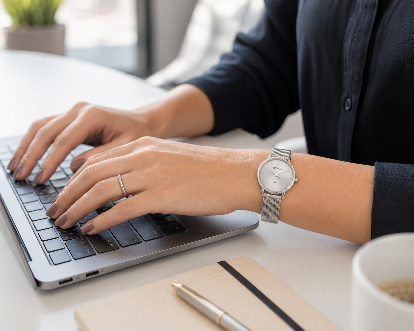 Mulher digitando em um laptop usando relógio feminino Seculus com pulseira mesh de aço e mostrador analógico, em ambiente de escritório moderno com iluminação natural e estilo clean.