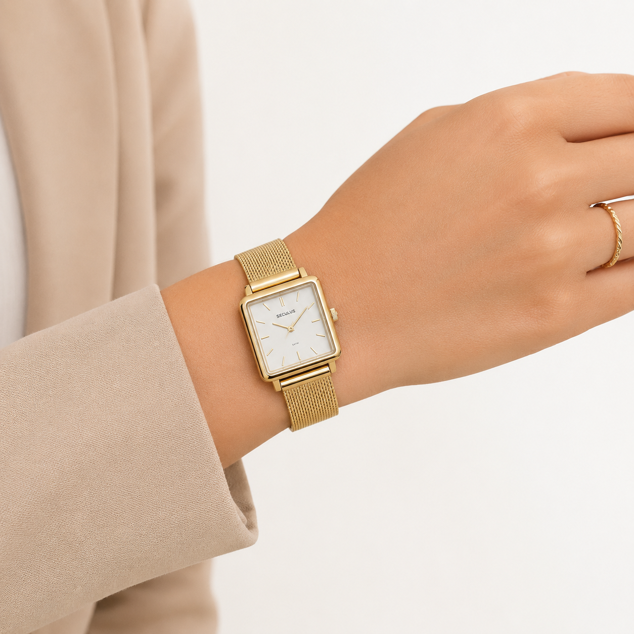 Pulso feminino usando relógio Seculus quadrado dourado com pulseira de malha de aço, combinado com anel fino dourado e manga de blazer bege, em estilo minimalista sofisticado.